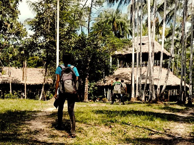 Persona caminando con morral hacia una maloca en la selva
